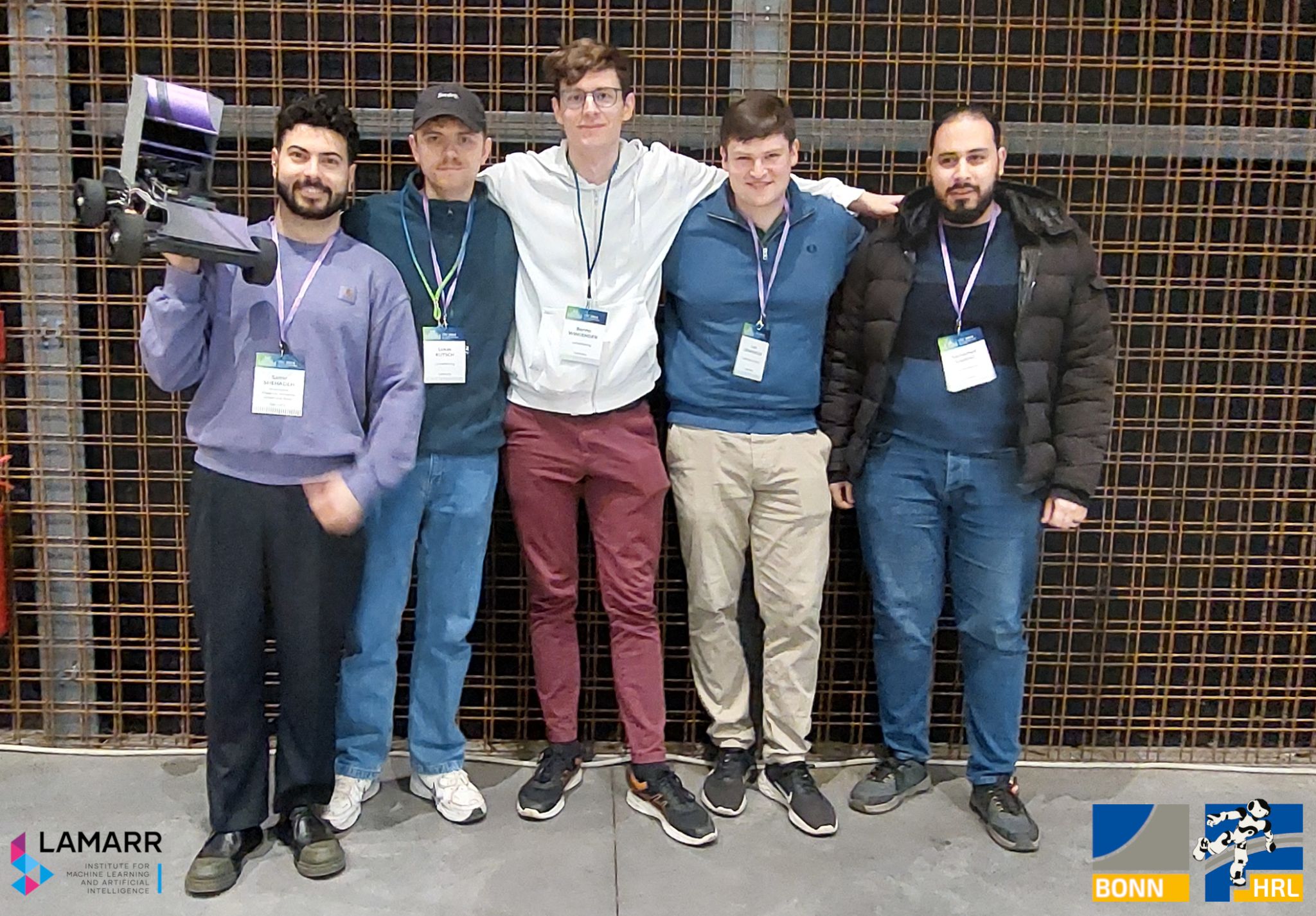 LAMARRacing team at CDC 2024: Samer Shemalleh, Lukas Kutsch, Bennett Wiegard, Luis Denninger, and Moein Eskandari with the robot car in front of the Lamarr Institute and HRL Bonn logos